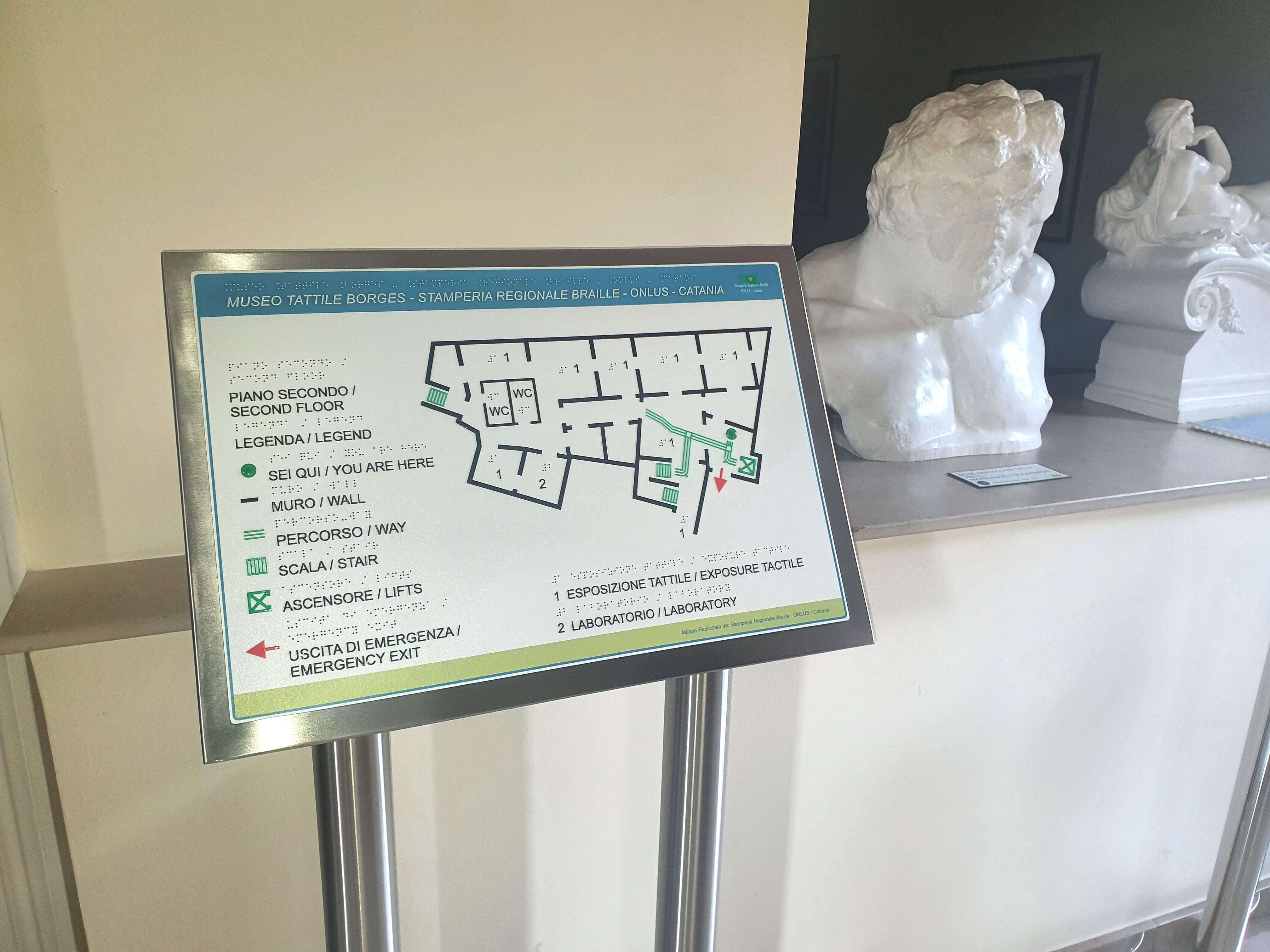 Mappa tattile del secondo piano del Museo Tattile Borges di Catania, situata accanto a busti scultorei bianchi.
