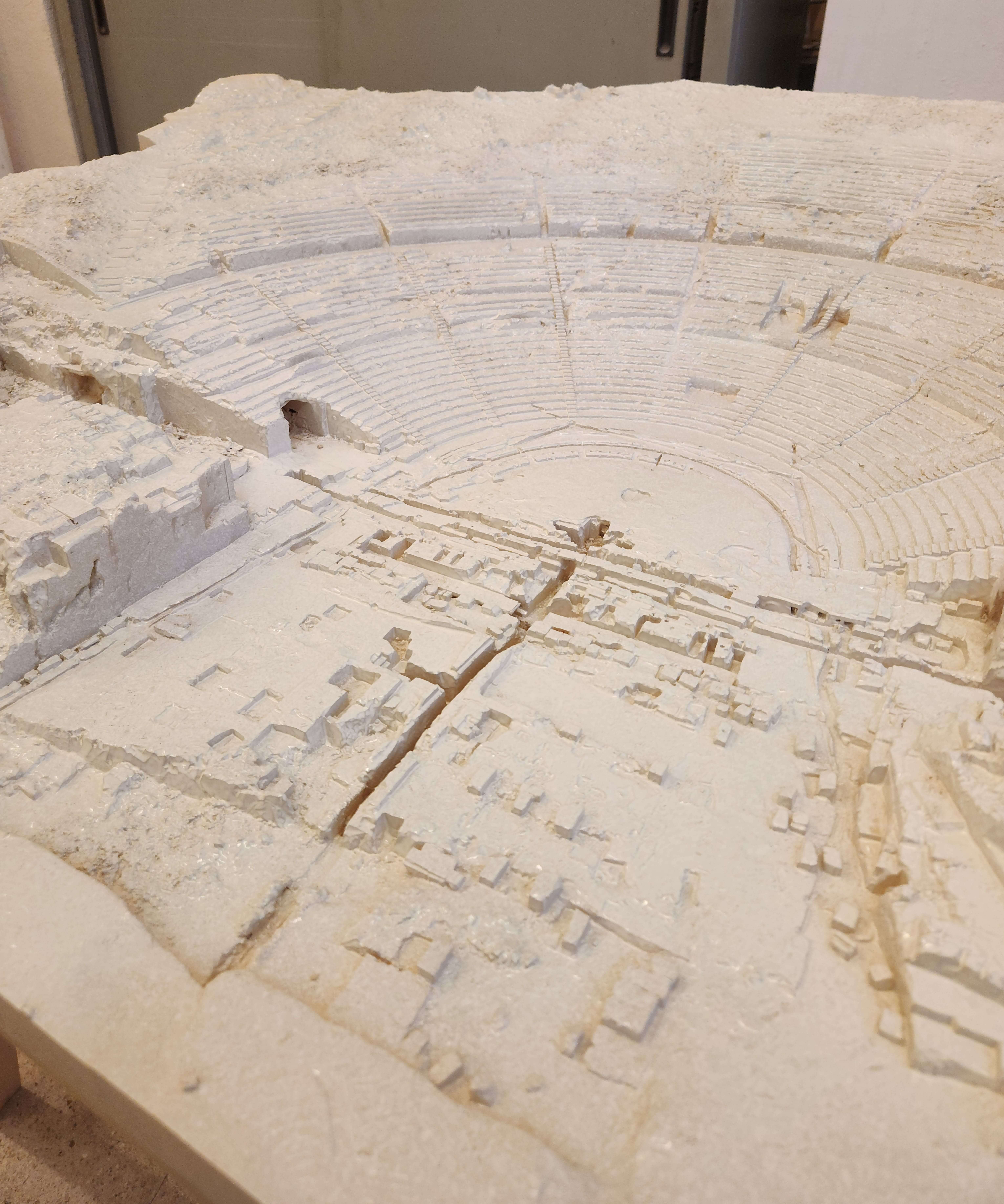 Ricostruzione plastica monocromatica di un antico teatro greco, con dettaglio delle gradinate e dell'area del palcoscenico.