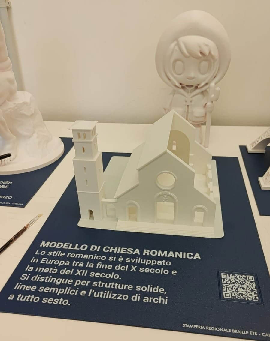 Modello didattico bianco di una chiesa romanica con campanile, accompagnato da un pannello esplicativo con QR code.