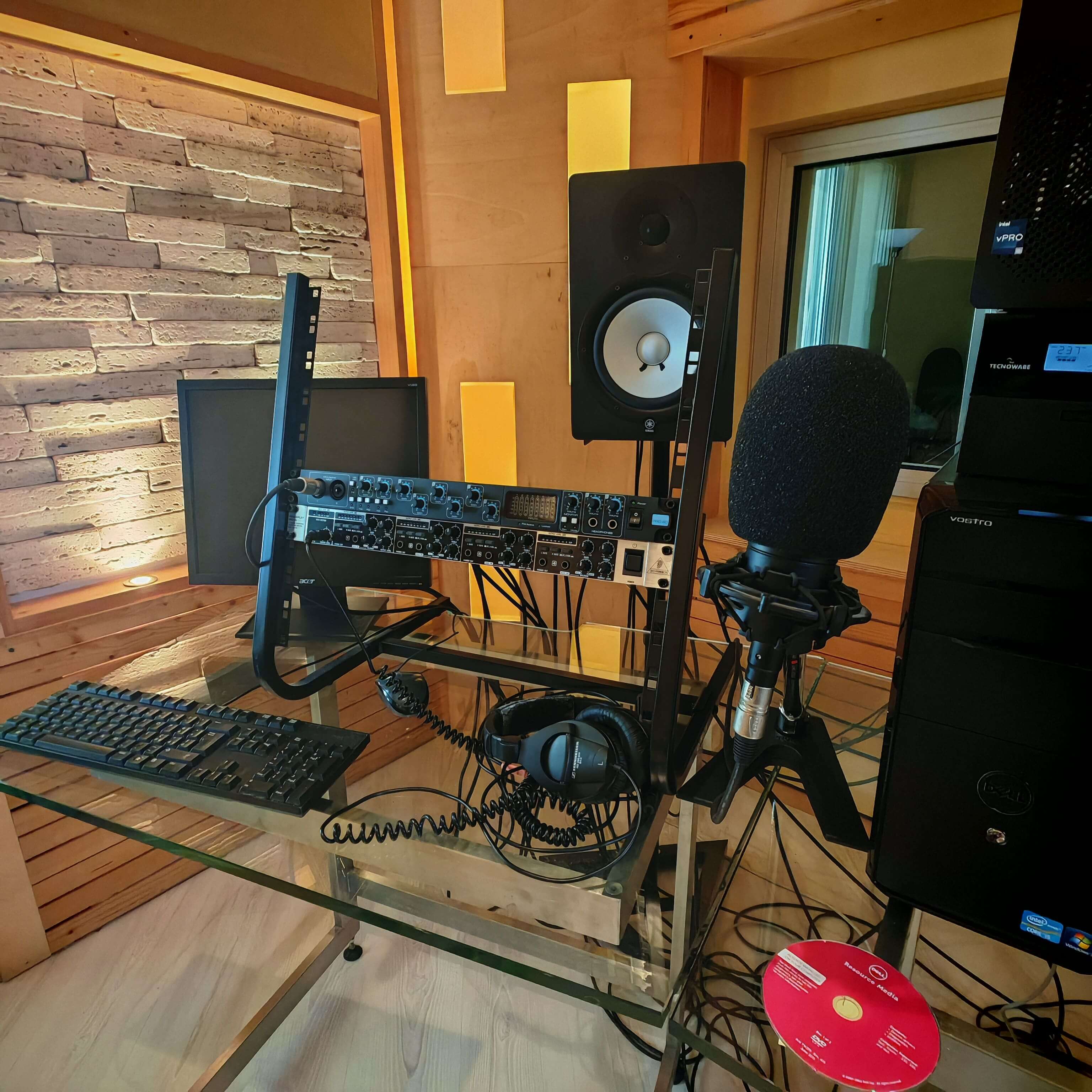 Dettaglio dell'attrezzatura di registrazione con microfono professionale dotato di filtro antipop, cuffie e interfaccia audio su scrivania.
