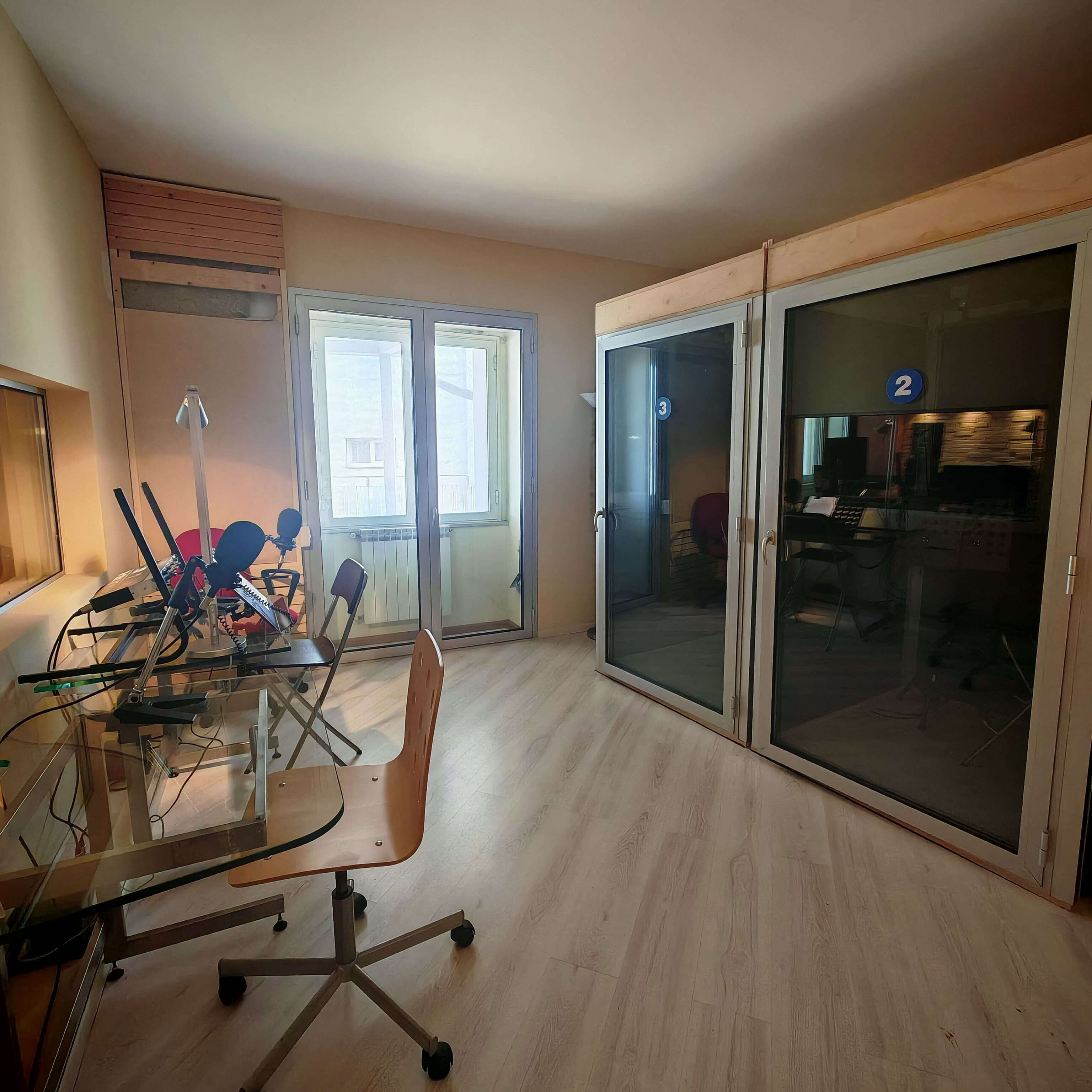 Interno dello studio con postazioni di lavoro e cabine di registrazione insonorizzate numerate per il doppiaggio o speakeraggio.