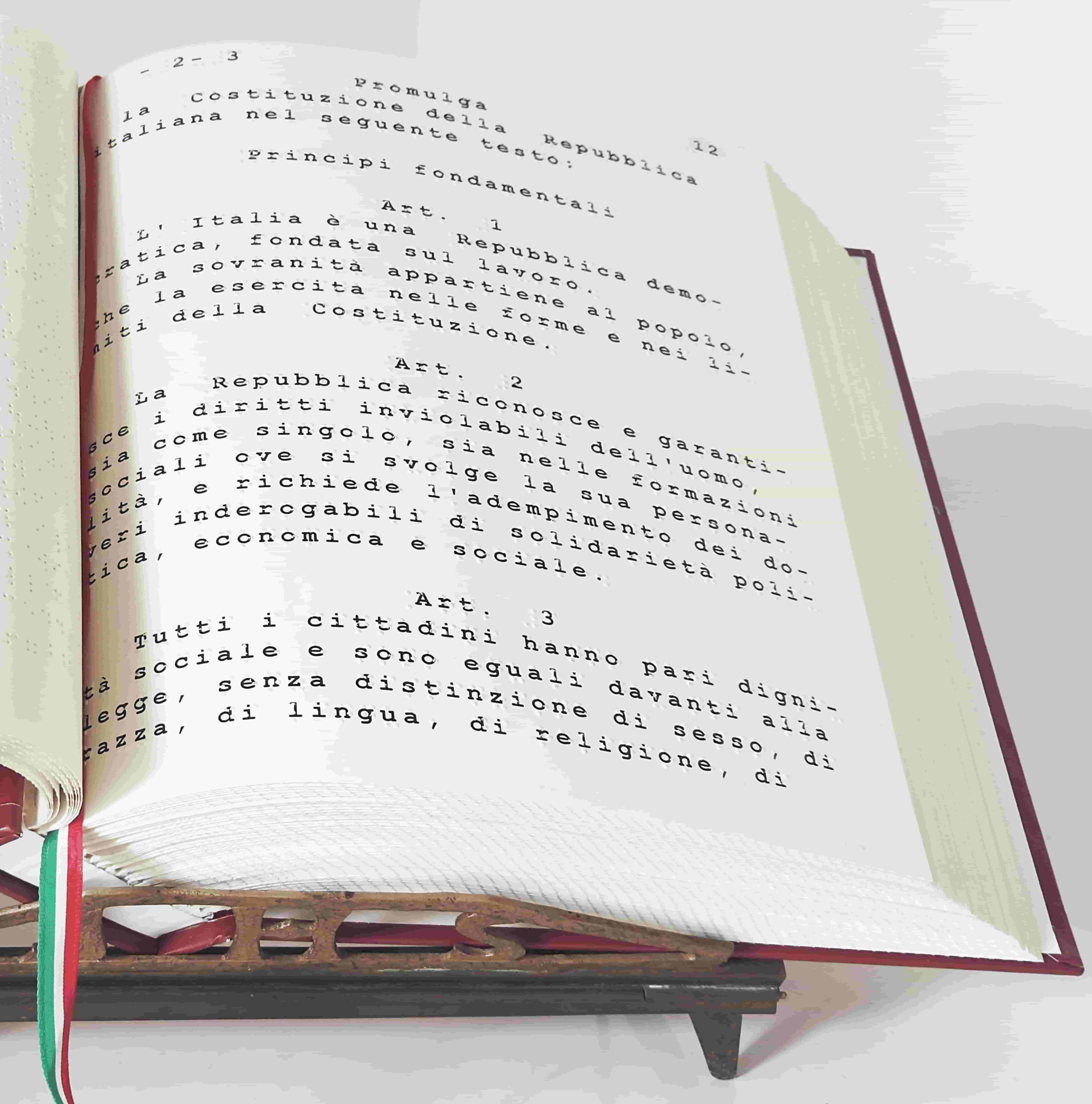 Volume della Costituzione Italiana aperto sui primi tre articoli, stampato in grandi caratteri ad alta leggibilità.