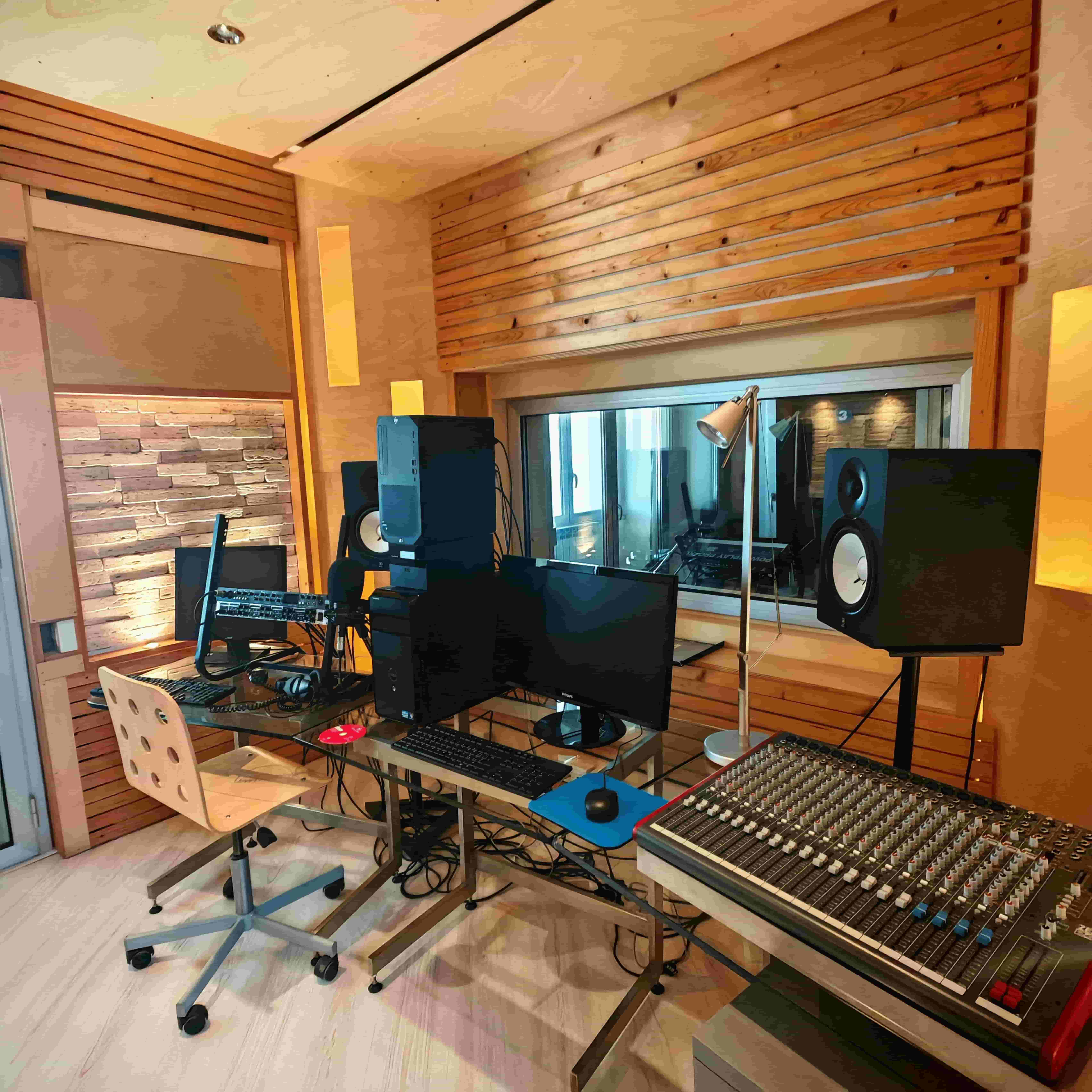 Interno di uno studio di registrazione audio con mixer professionale, monitor e pannelli in legno per il trattamento acustico.