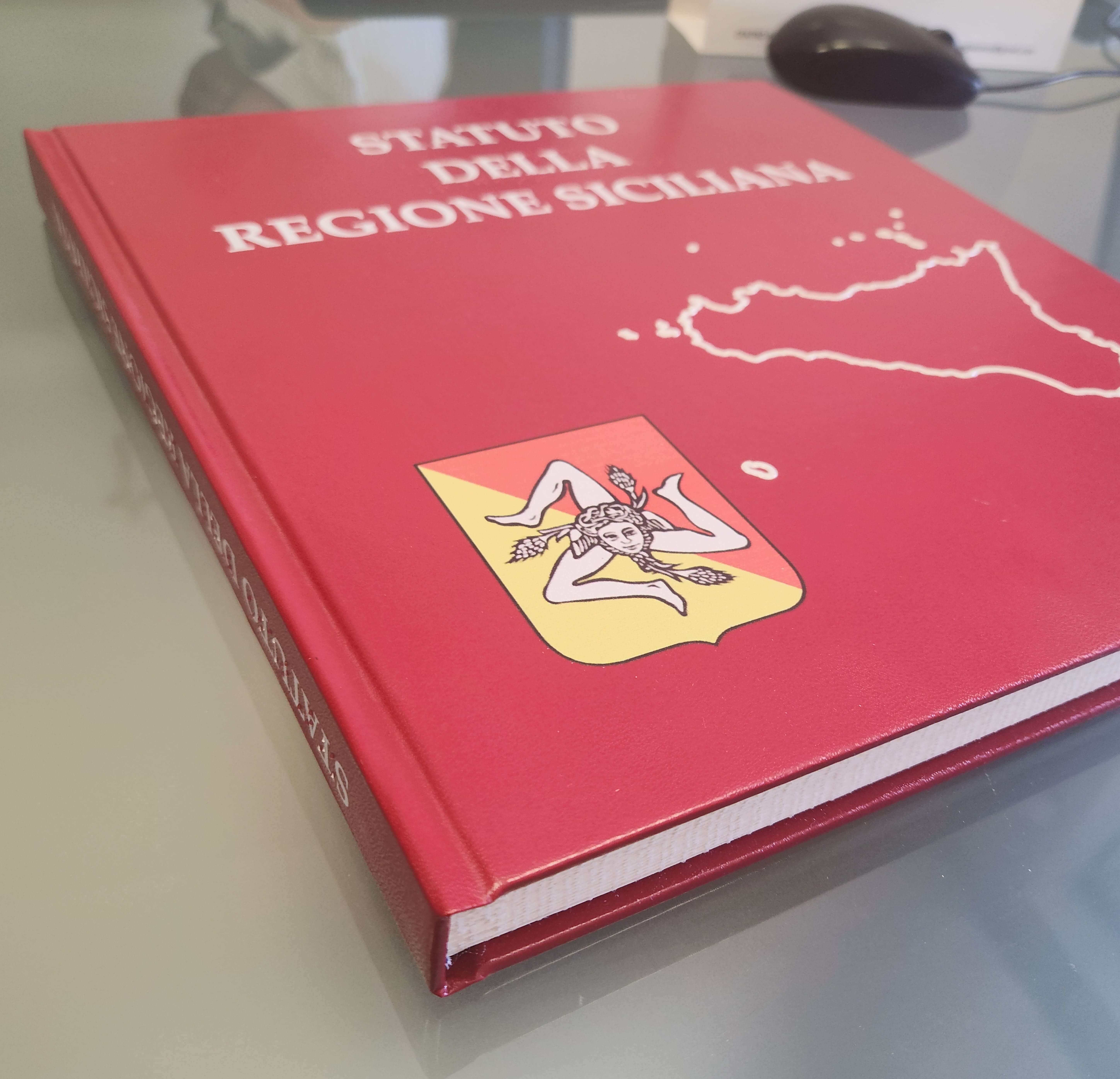 Copertina rossa del volume 'Statuto della Regione Siciliana' con stemma della Trinacria e contorni della Sicilia.