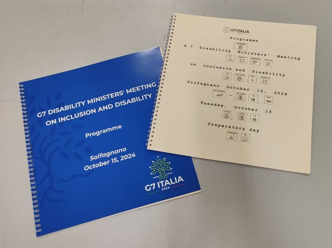 Manuali del G7 Disability Ministers' Meeting 2024 in versione blu standard e versione bianca accessibile con Braille.