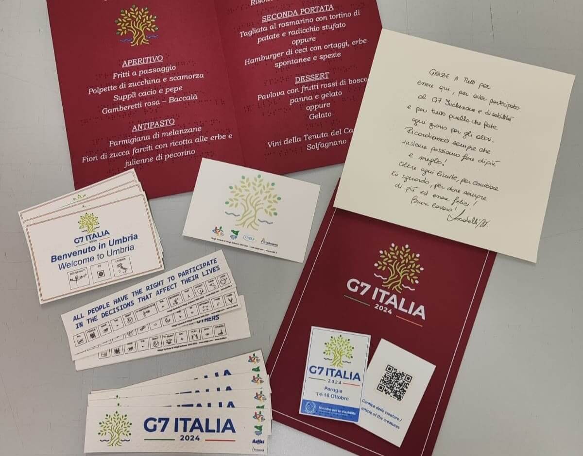 Kit di benvenuto del G7 in Umbria con menù, cartoline e badge stampati in formato accessibile nero-Braille.